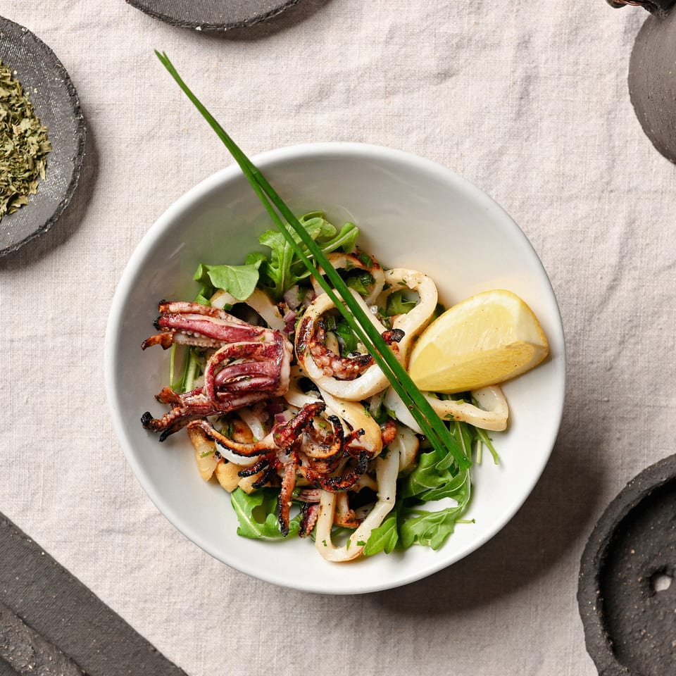 Grilled calamari and tentacles on a bed of arugula with a lemon wedge and chives.