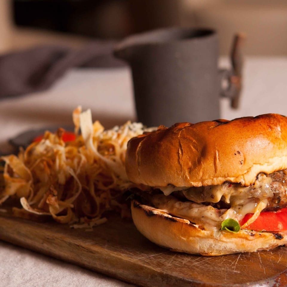 Gourmet burger with melted cheese, tomato, and lettuce, served with crispy fries on a wooden board.