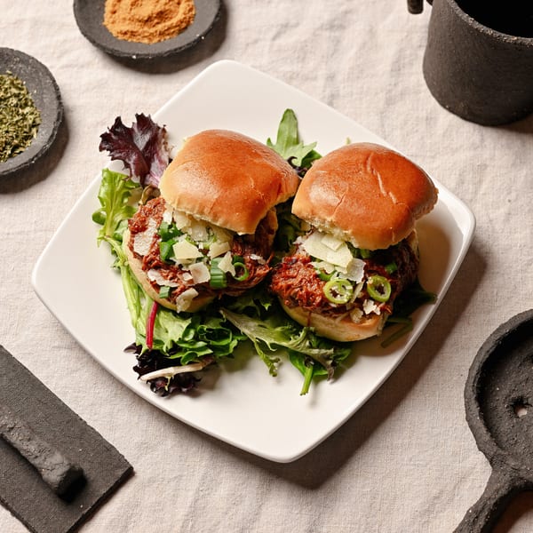 Two pulled pork sliders with cheese and green onions on a bed of lettuce.