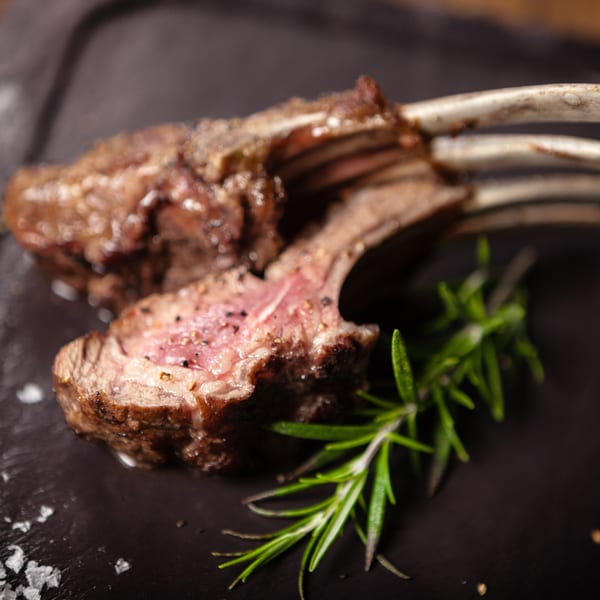 Two perfectly cooked lamb chops with rosemary and sea salt on a dark plate.